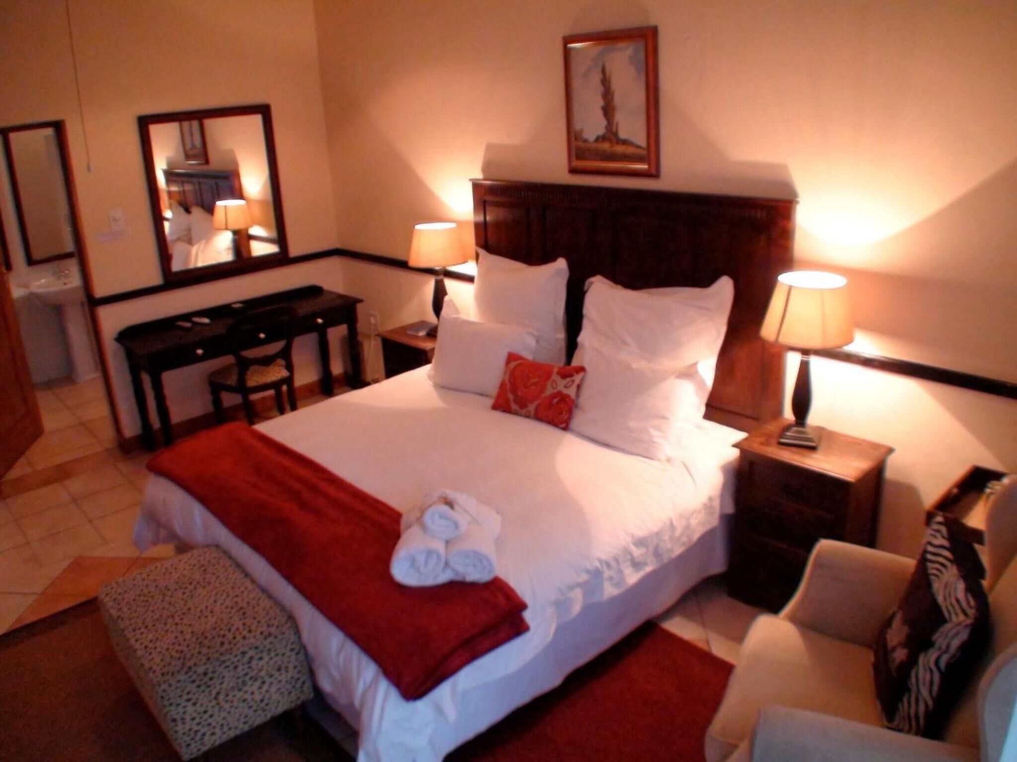 A hotel room with a bed, bedside tables, a desk, a chair, and a mirror.