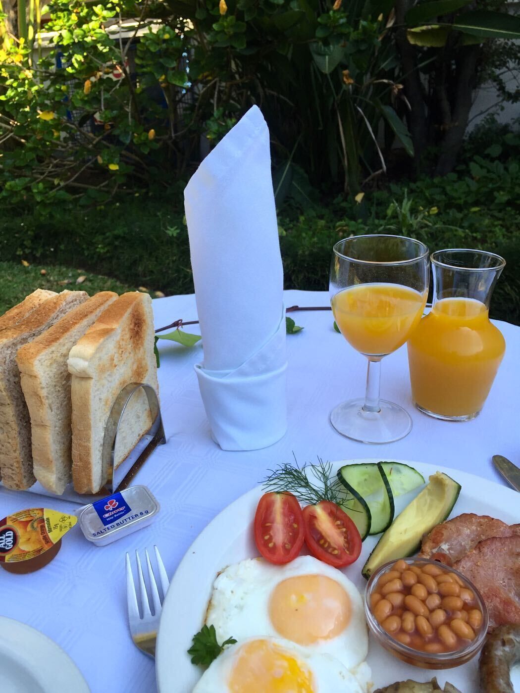 Ein Frühstückstisch mit Toast, Eiern, Tomaten, Gurken, Avocado, Bohnen und Saftgläsern.