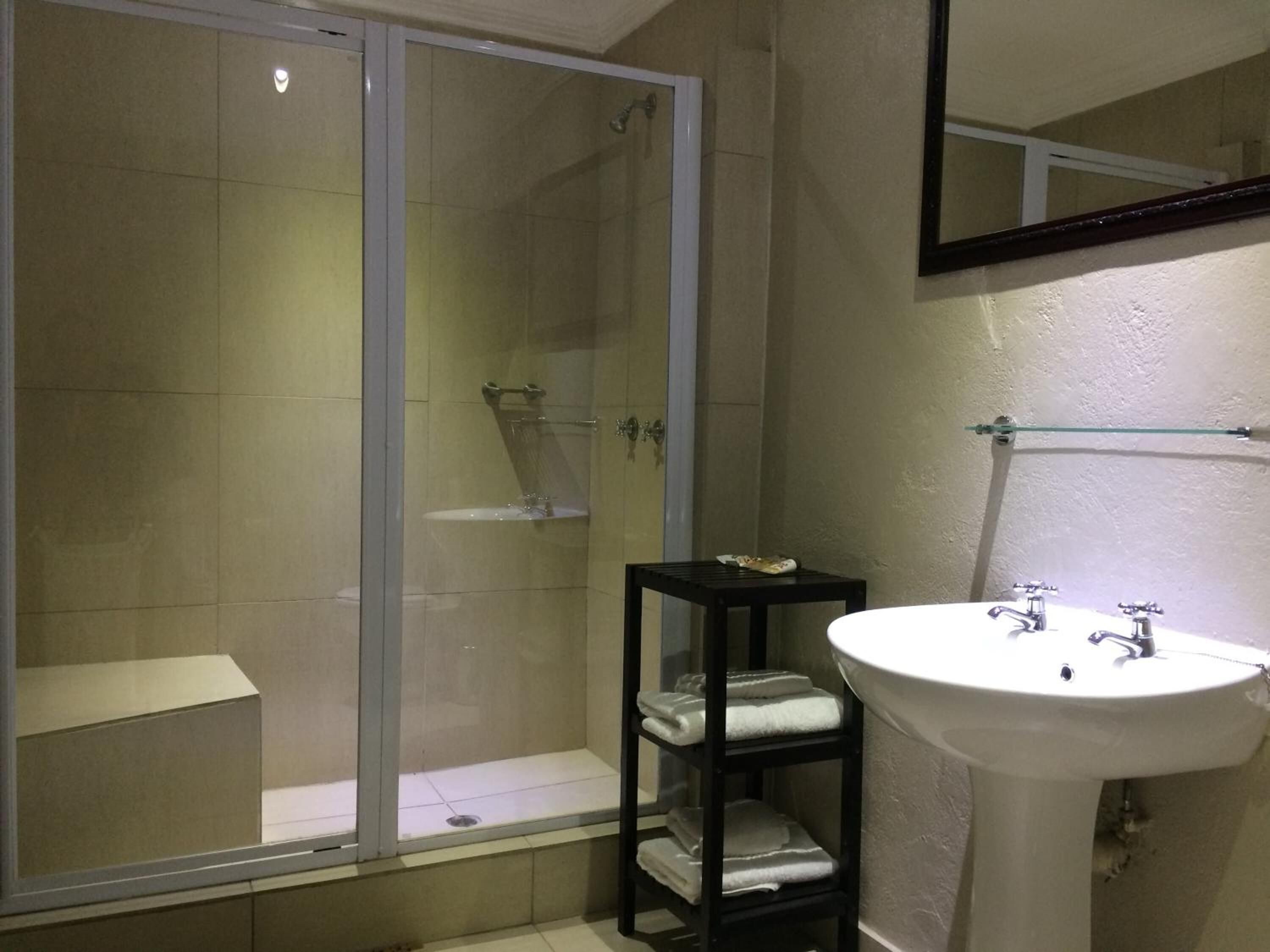 Une salle de bain avec une douche à parois de verre, un lavabo blanc et une petite étagère avec des serviettes.