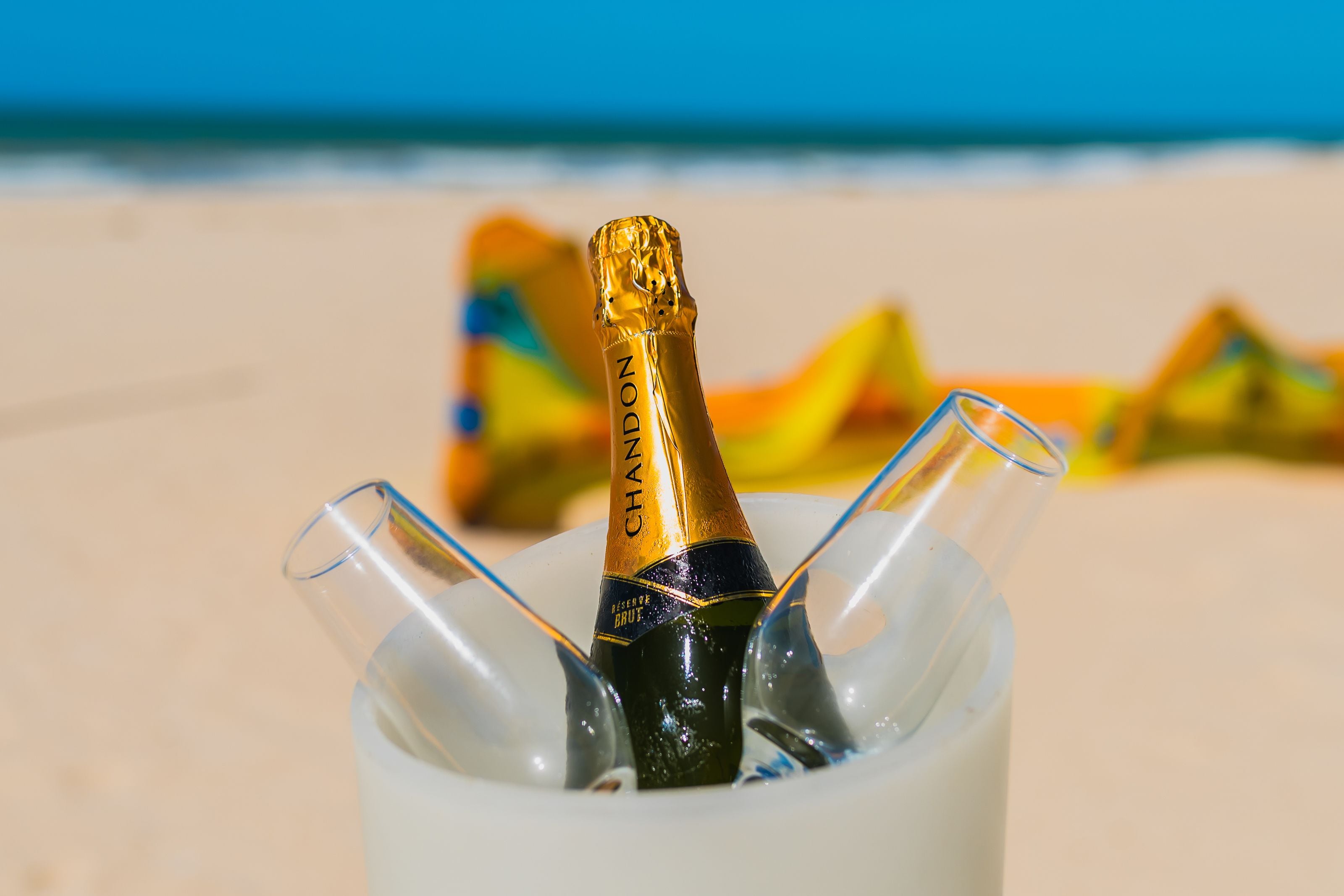 En champagneflaska i ett genomskinligt glasförvaringskärl på en strand.