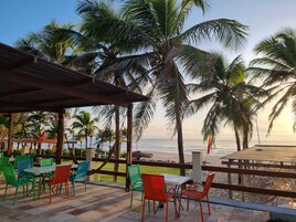 Un patio frente a la playa con mobiliario exterior y palmeras.