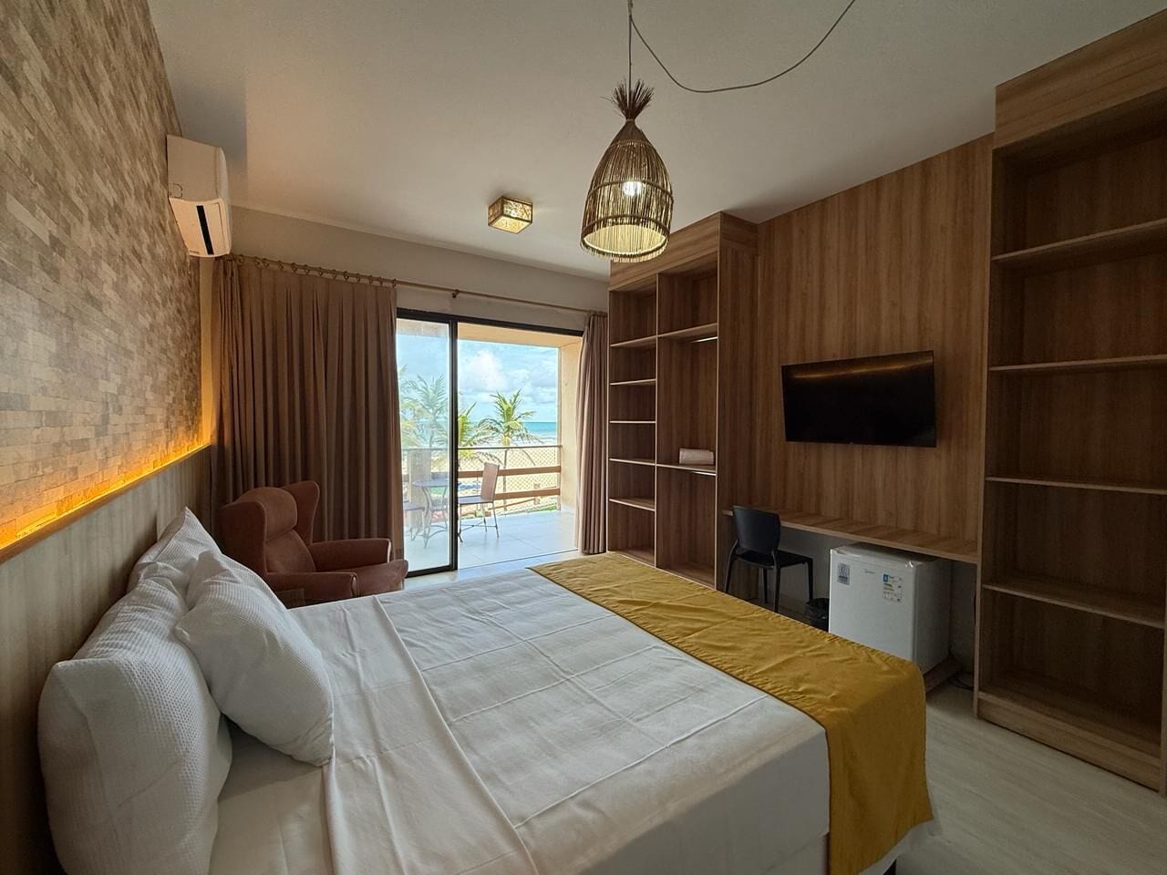 Habitación de hotel con cama, escritorio, televisor y balcón con vistas.