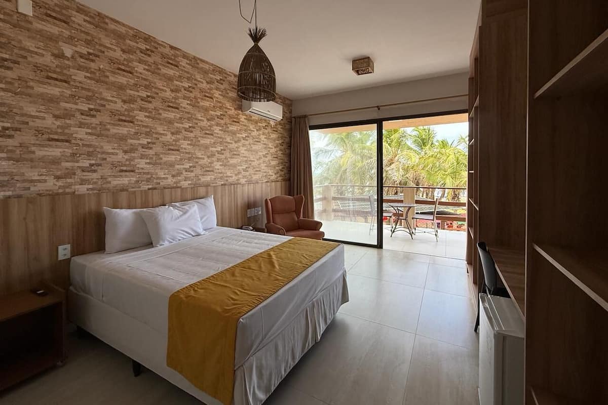 A bedroom with a bed, a chair, a TV, a wardrobe, and a balcony with outdoor furniture.