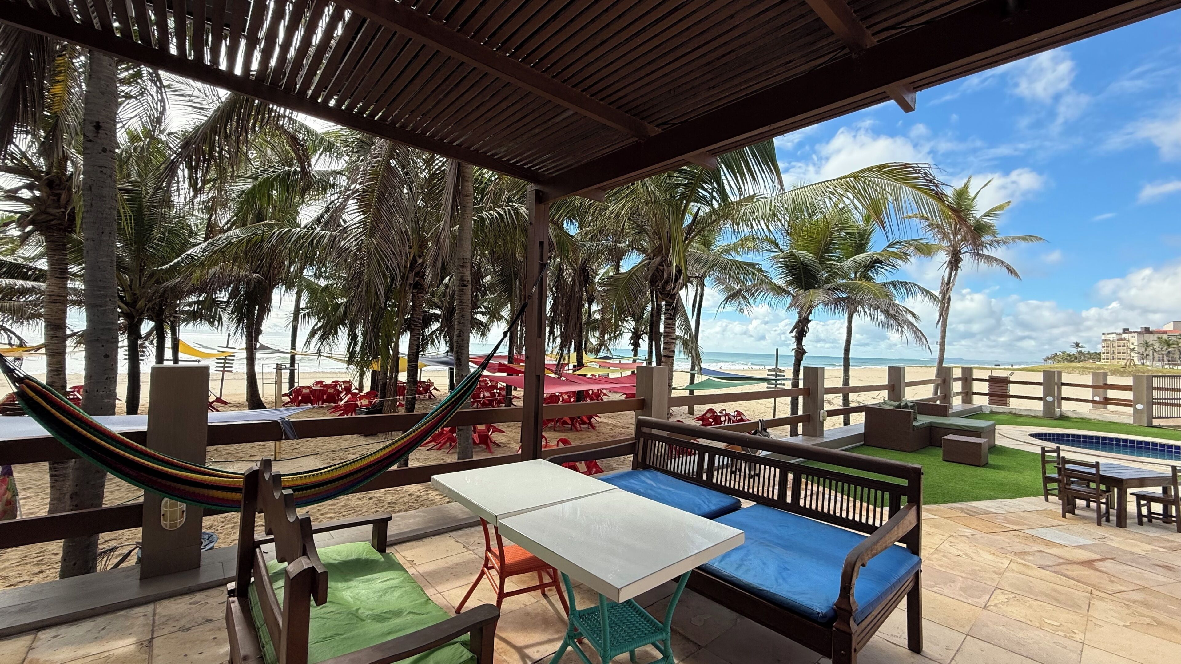 Un espace extérieur abrité, avec des tables et des bancs, un hamac, et une vue sur la plage et l’océan.