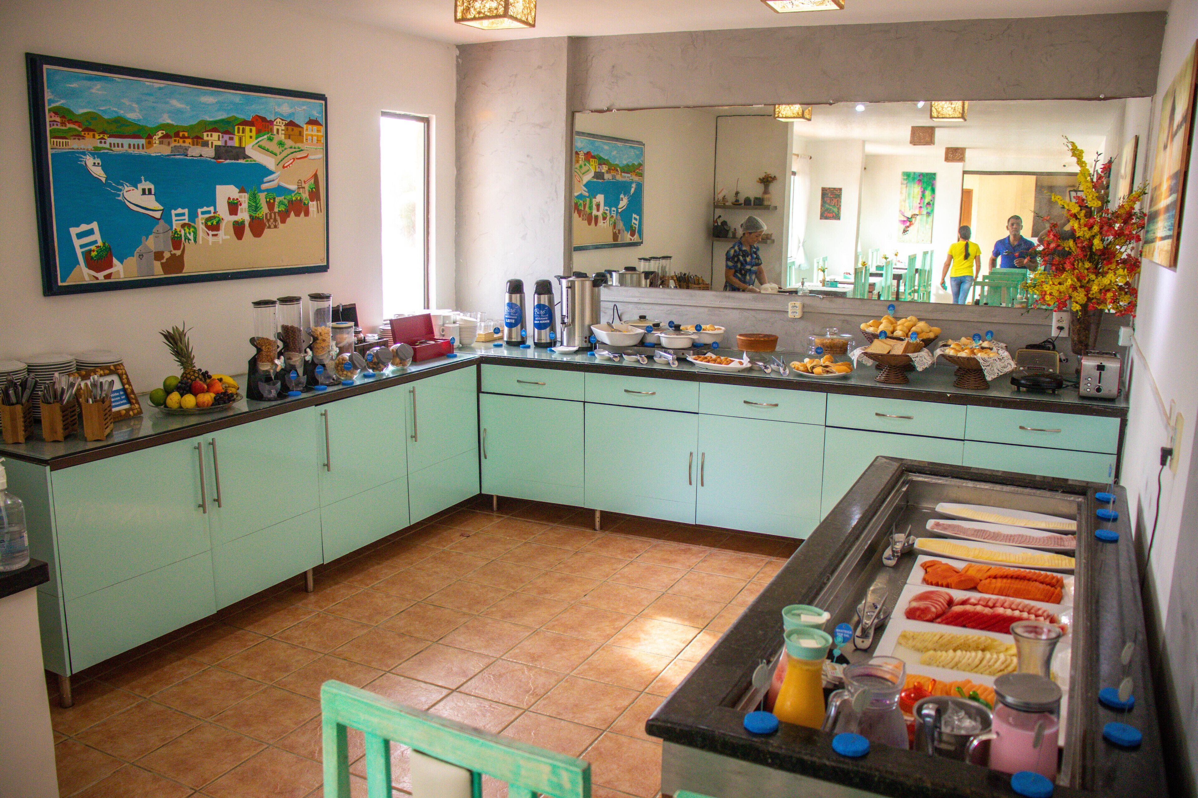 A kitchen with light green cabinets, a tiled floor, and a buffet counter with various food items.