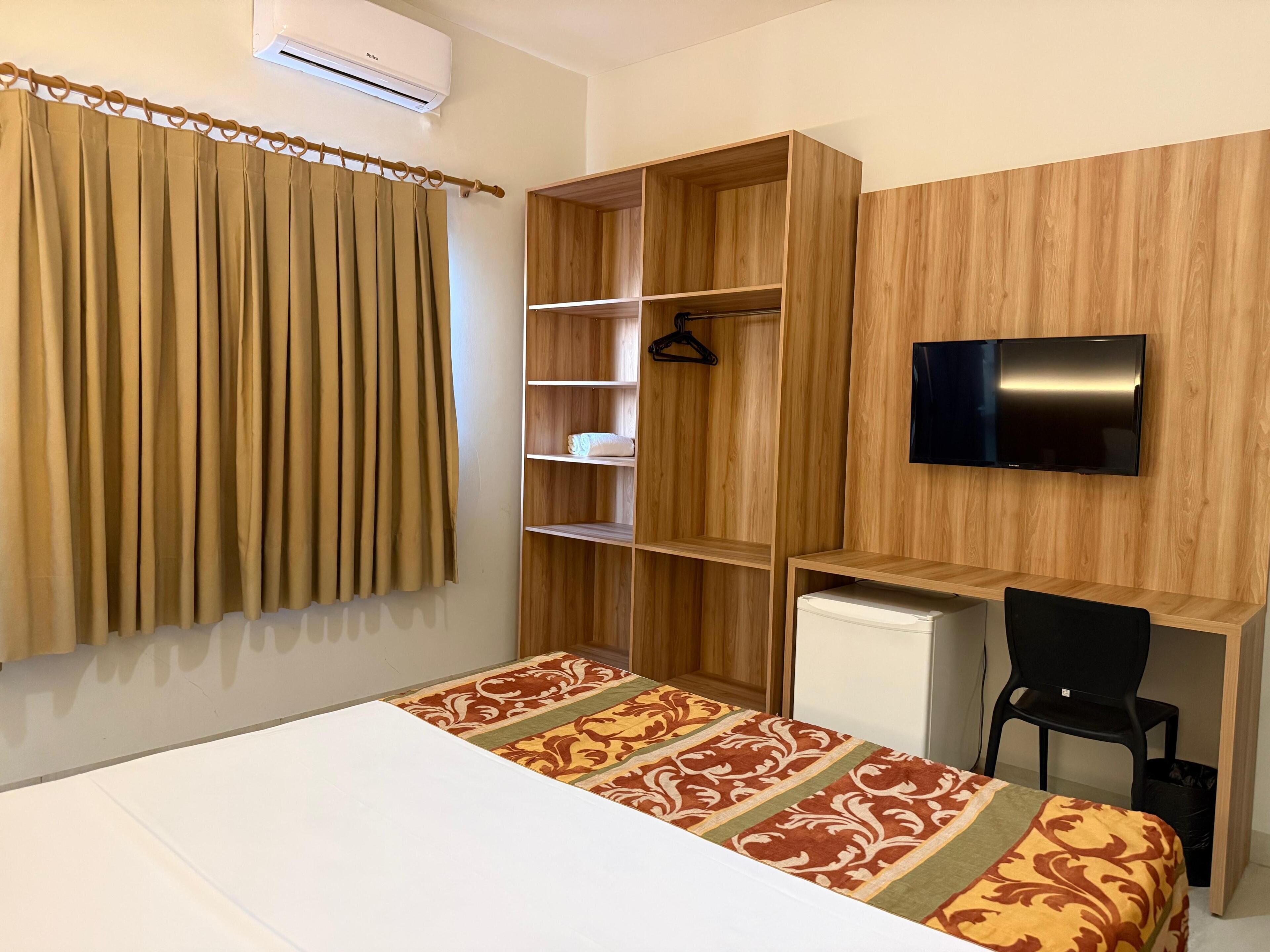 A bedroom with a bed, a desk, a chair, a TV, and a wardrobe.