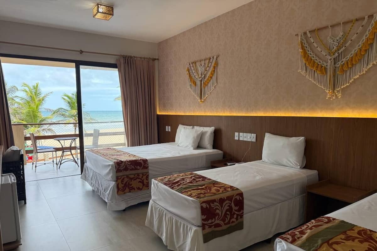 A hotel room with three beds, a balcony with a view of the beach, and a dining area.