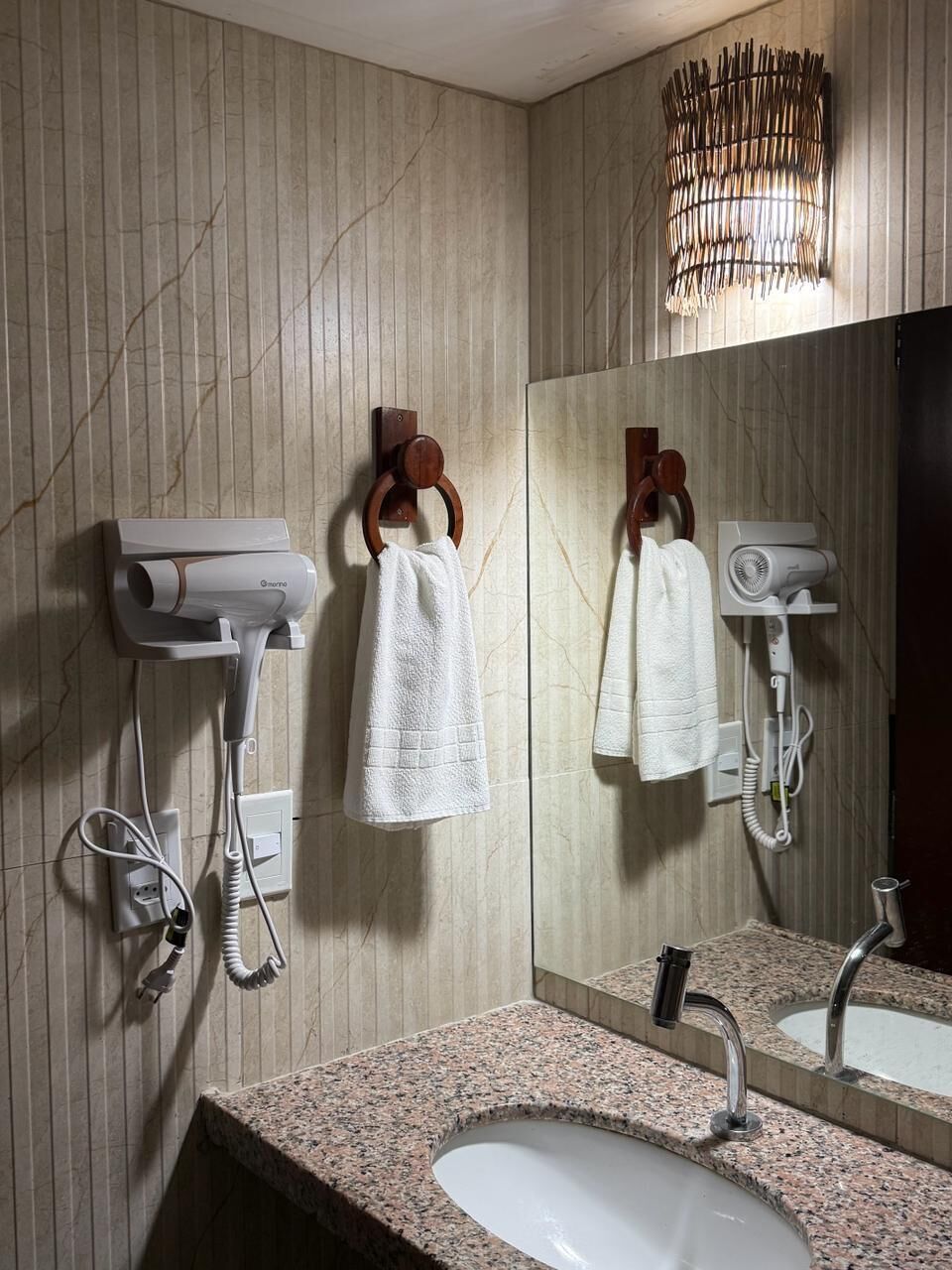 Un baño con encimera de granito, un lavabo, un espejo, un perchero para toallas y dos secadores de pelo montados en la pared.