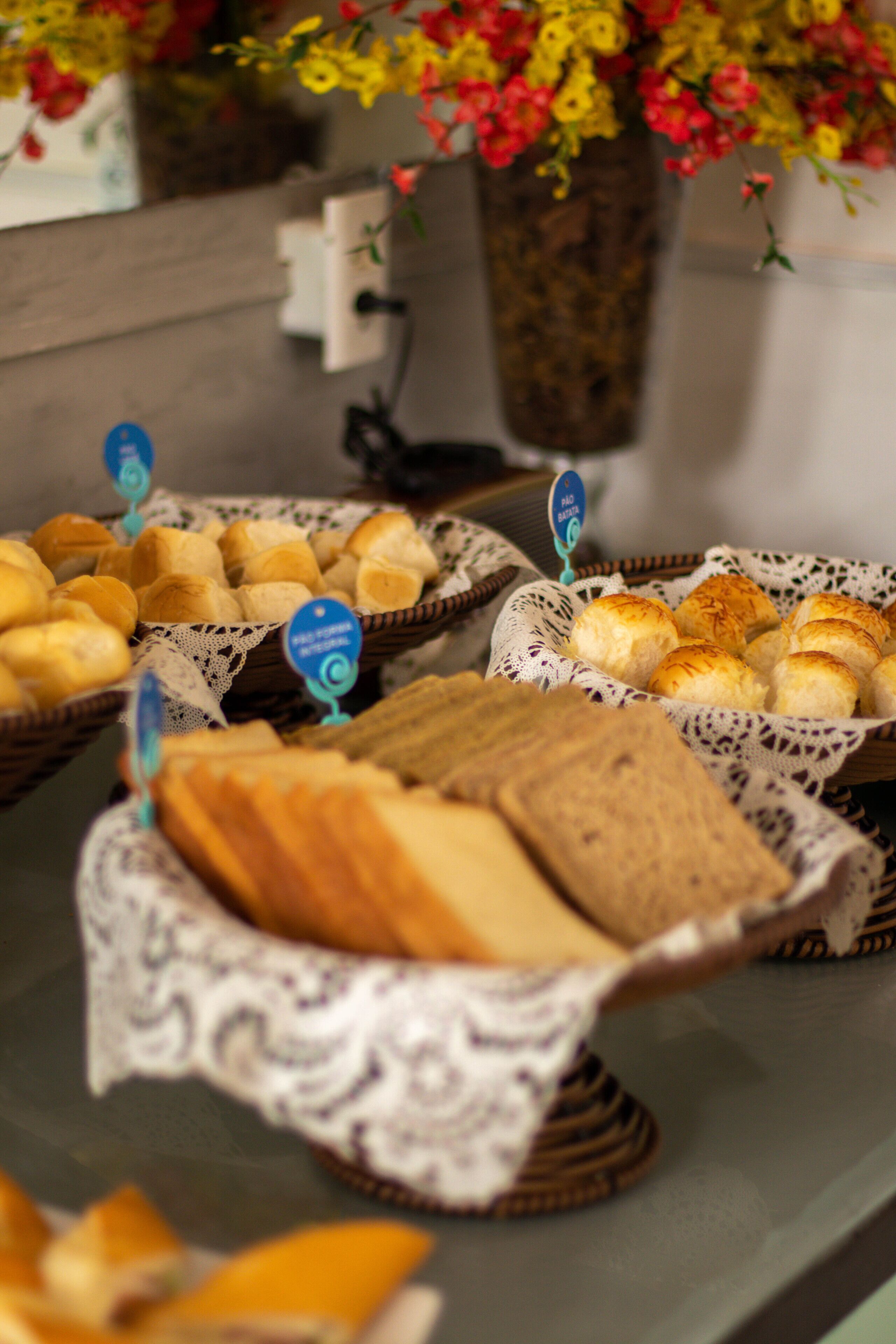 A buffet table with various breads and pastries in baskets, with a floral arrangement in the background.