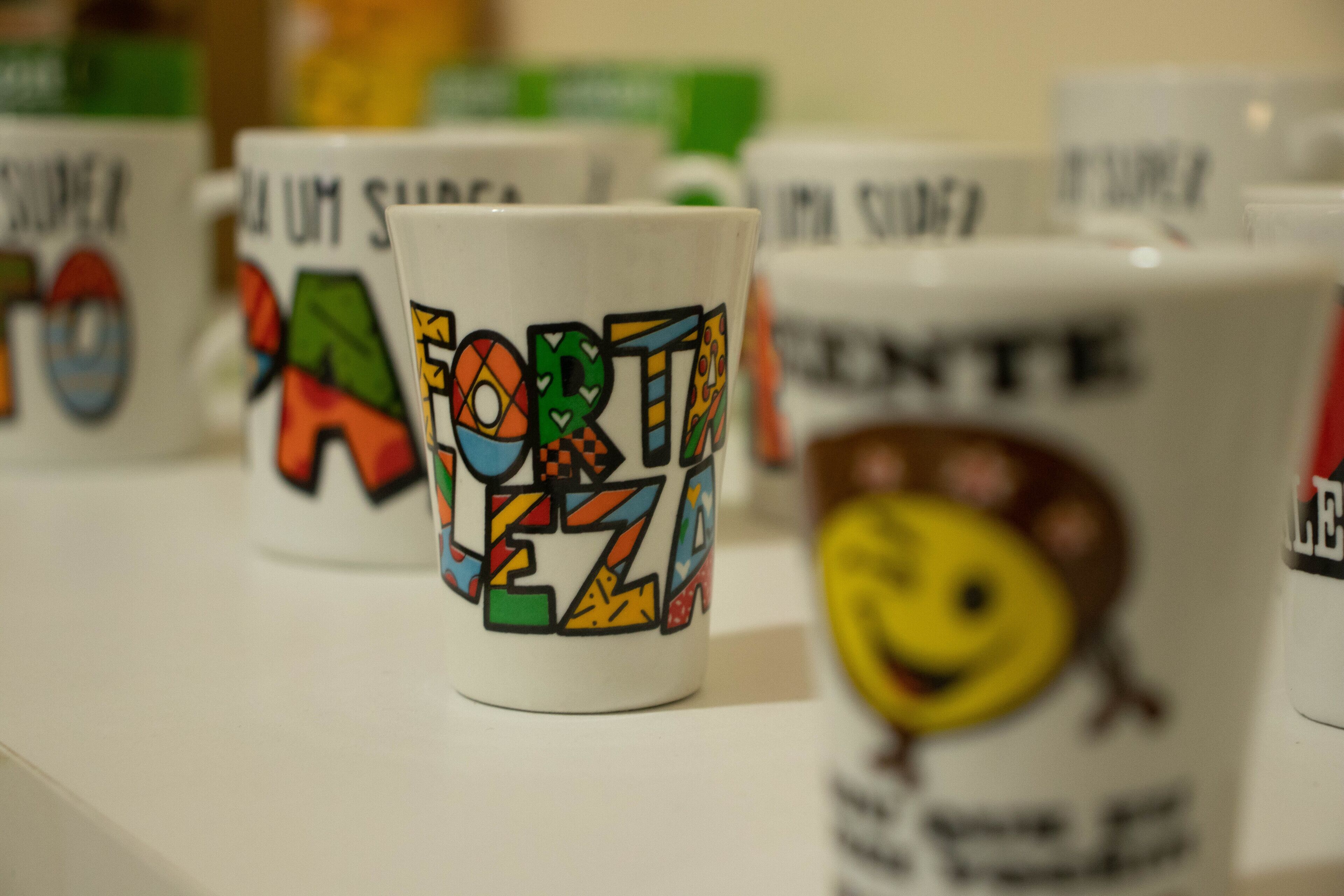 A row of white mugs with colorful designs and text.