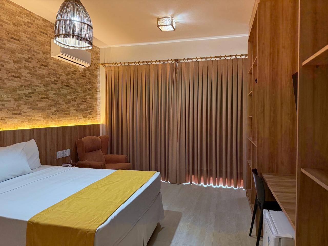 Una habitación de hotel con cama, una silla, un armario y una cortina.