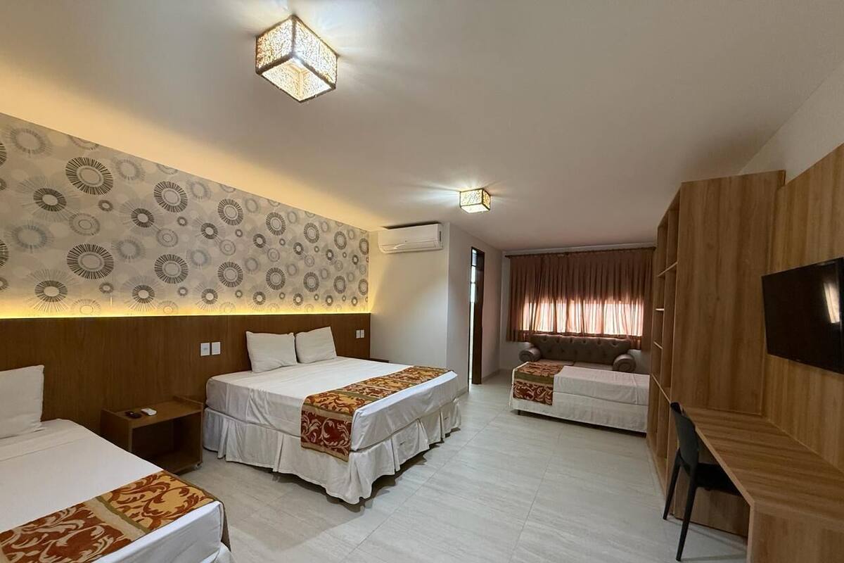 A hotel room with two beds, a desk, a TV, and a patterned wall.