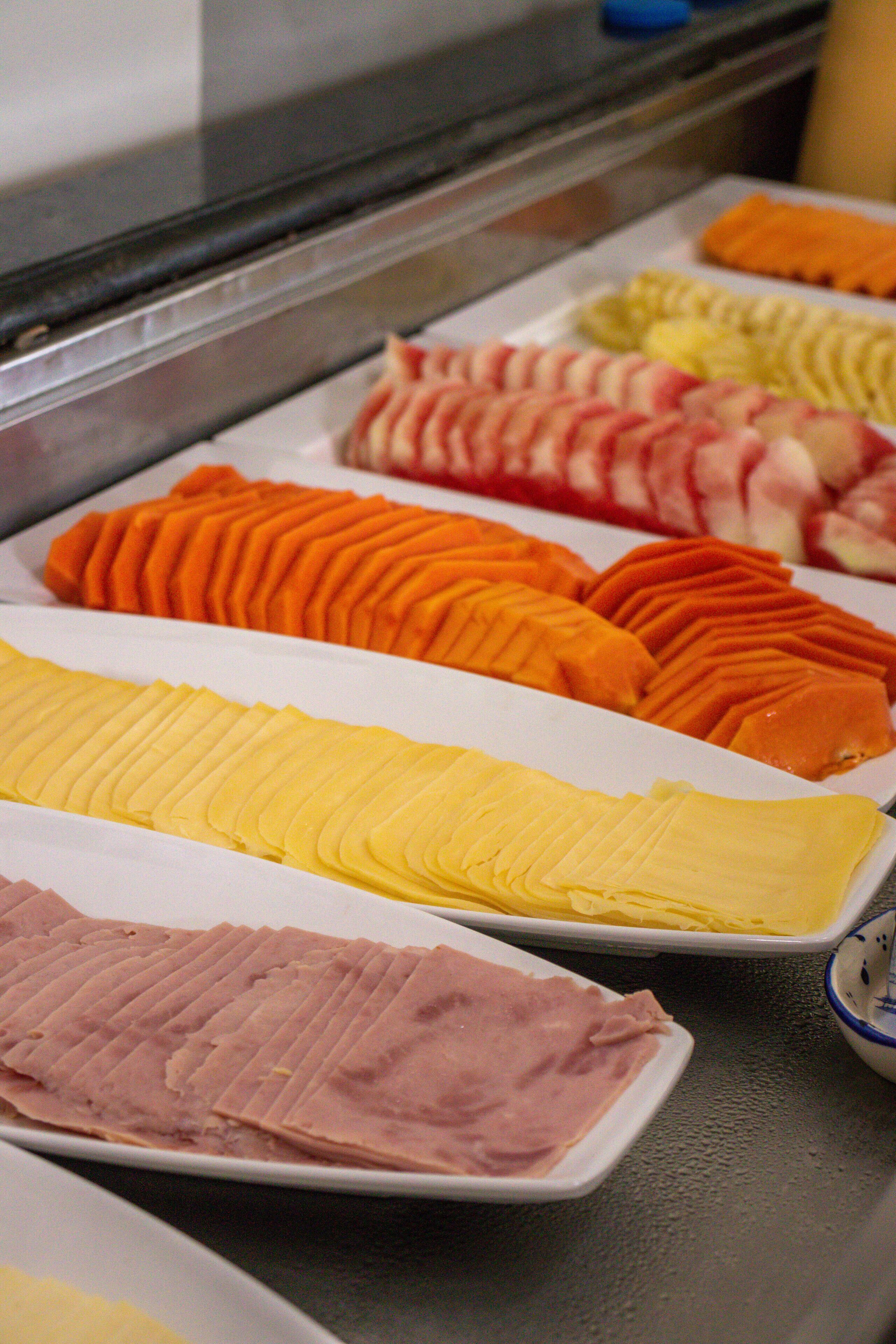 A display of sliced fruits and meats in a deli counter.