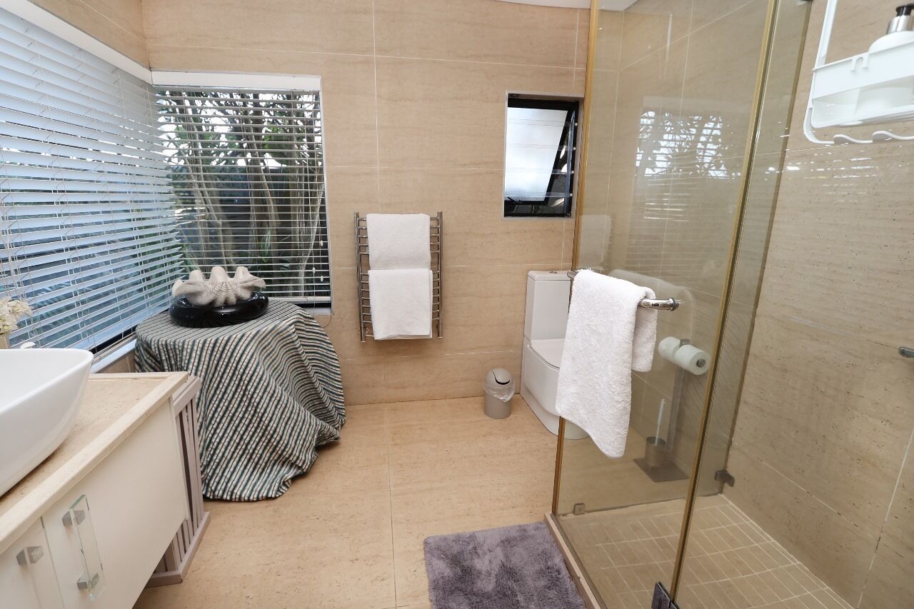 Un baño moderno con cabina de ducha de vidrio, un lavabo con una toalla a rayas y un taburete pequeño.