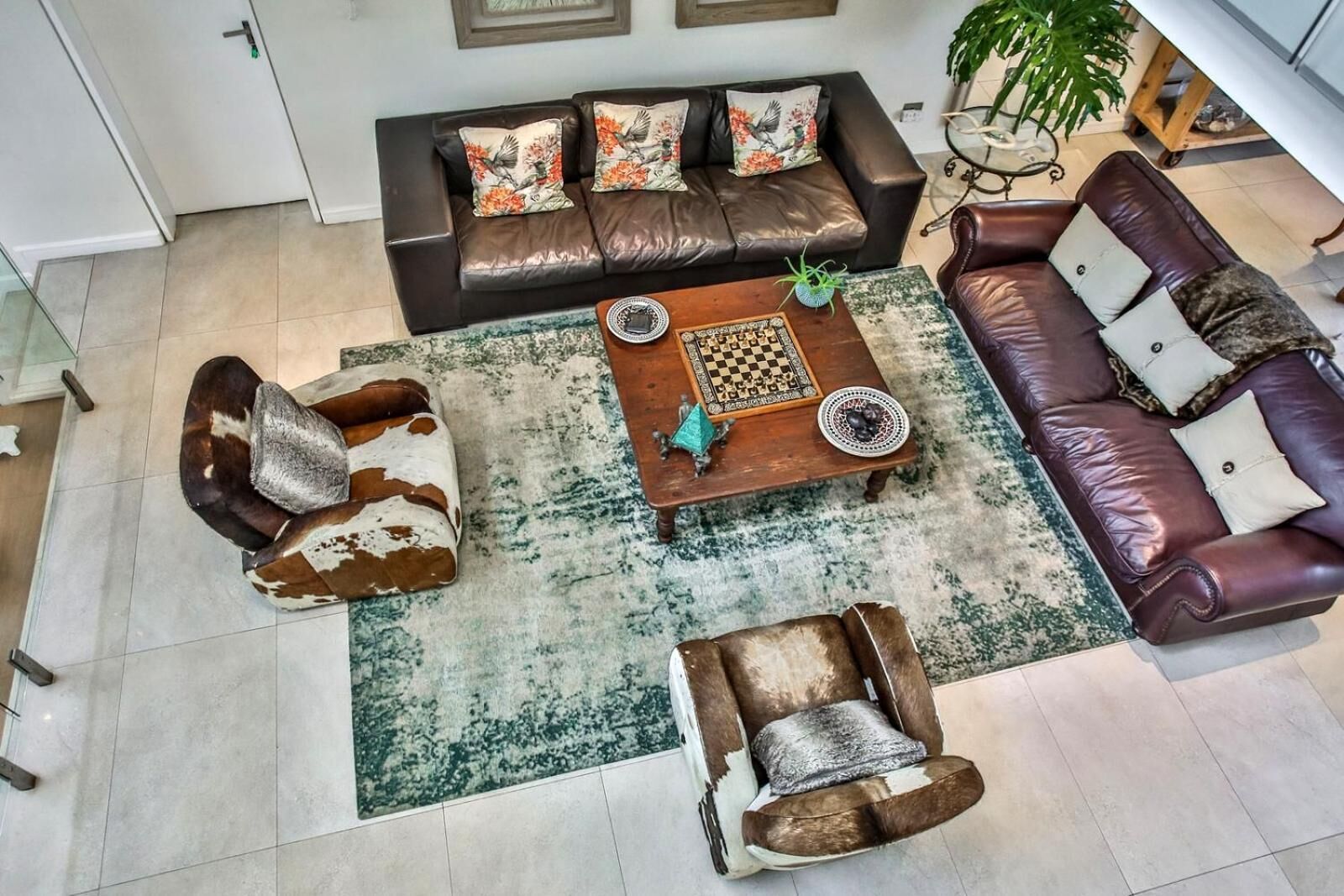 Uma sala de estar espaçosa com um sofá de couro marrom, uma poltrona combinando e uma mesa de centro com um tabuleiro de xadrez.