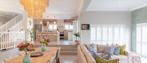 A spacious living area with a wooden dining table, a sofa set, and a chandelier.