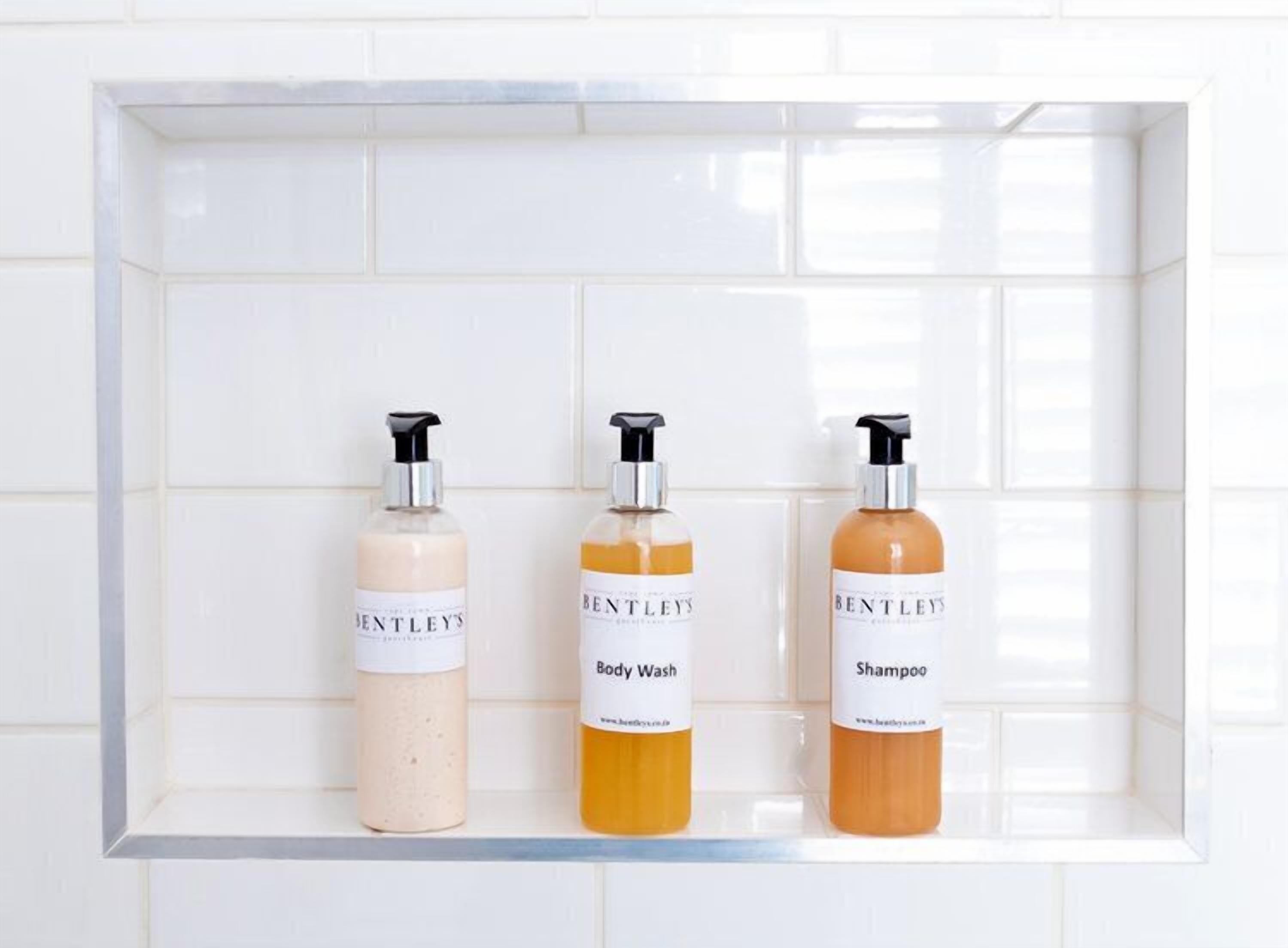 Three bottles of Bentley's Body Wash and Shampoo on a white tiled shelf.