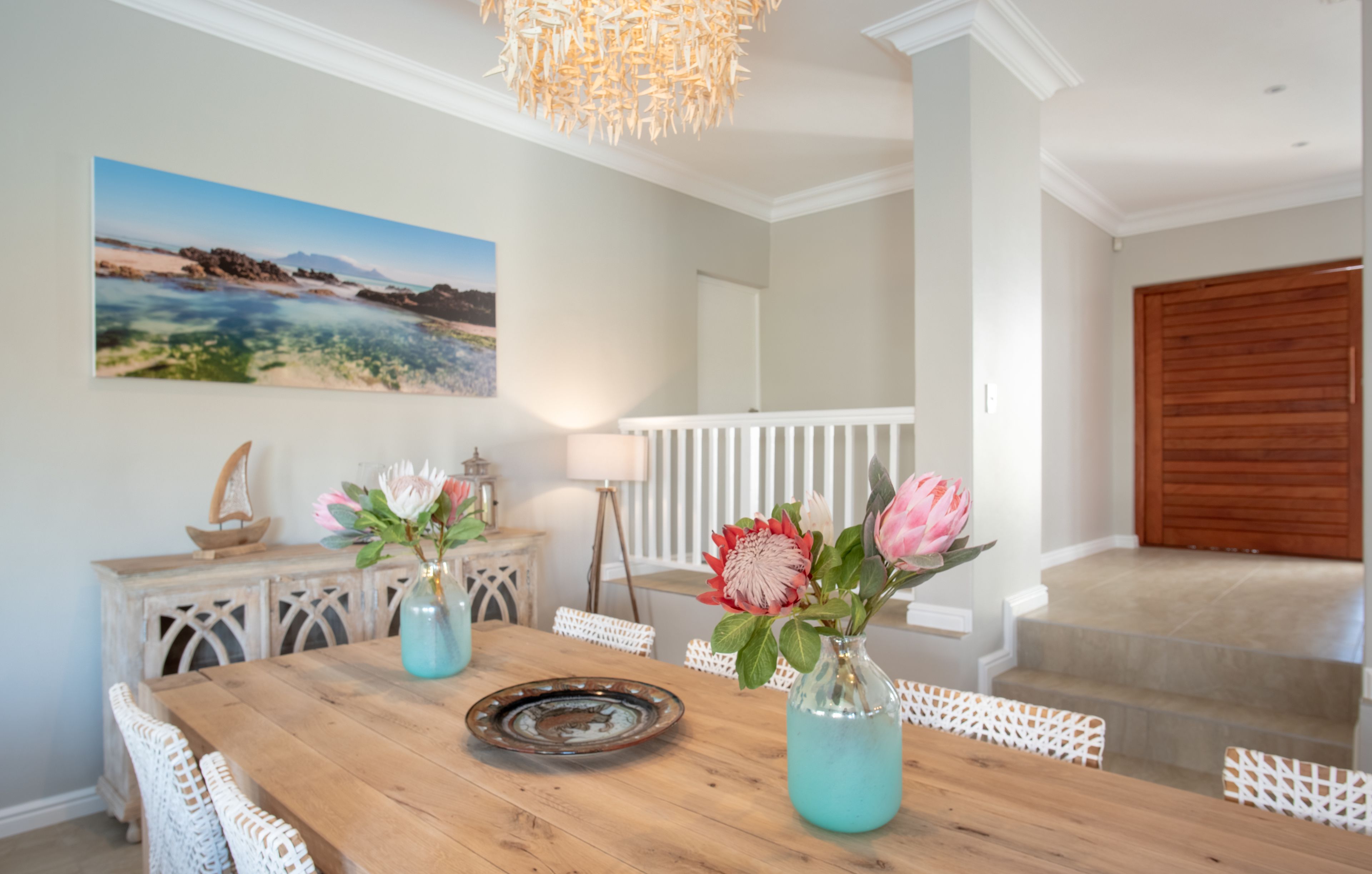 A dining area with a wooden table, white chairs, and two vases with flowers.