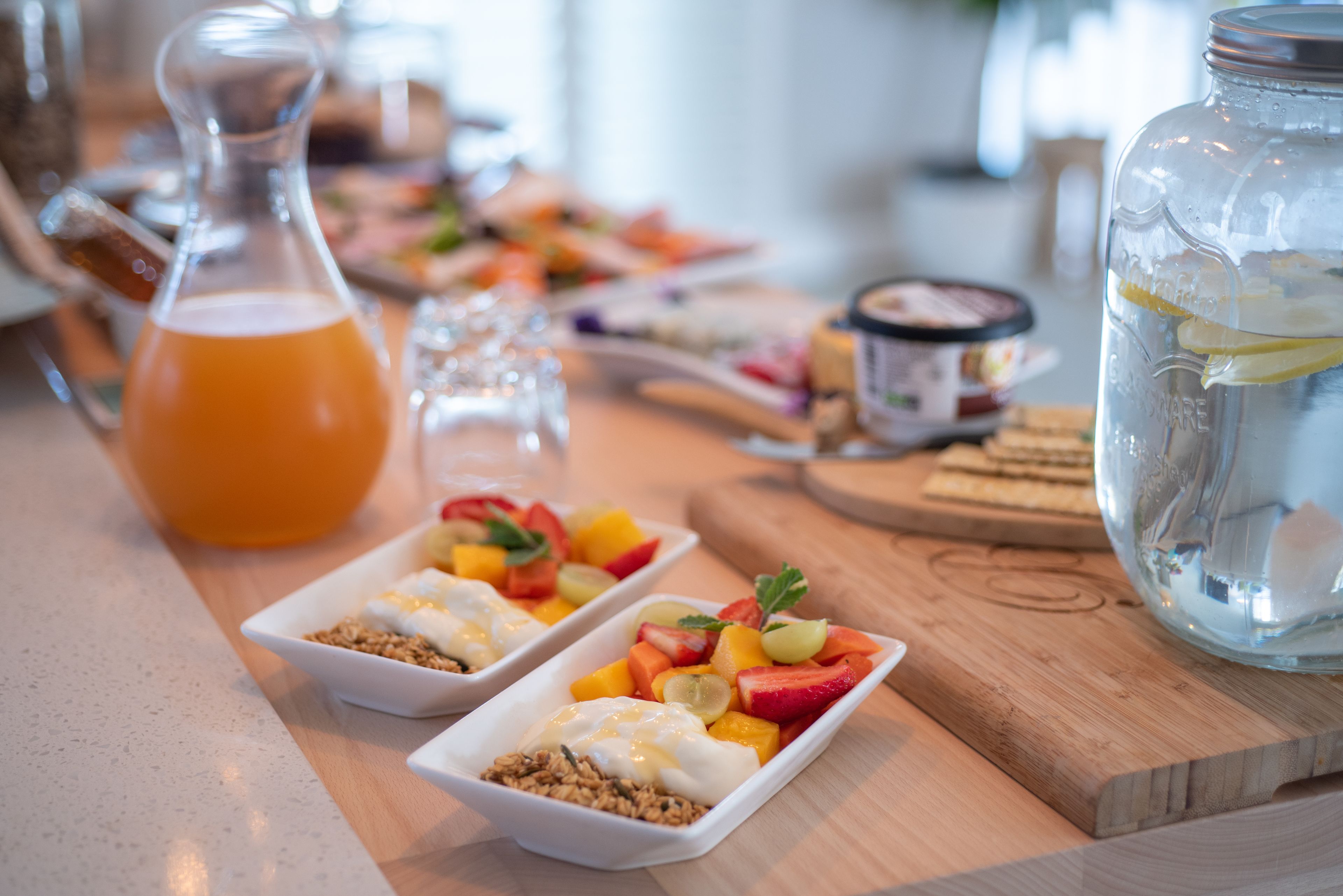 A breakfast buffet with various dishes, including fruit and yogurt parfaits, on a wooden table.