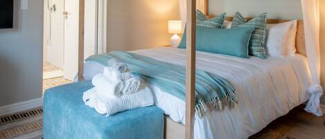 A bedroom with a four-poster bed, a bedside table with a lamp, and a rolled towel on the bed.