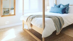 A four-poster bed with white bedding and blue pillows, a wooden floor, a large mirror, and a window with blinds. - Bentley's Guesthouse (Cape Town)