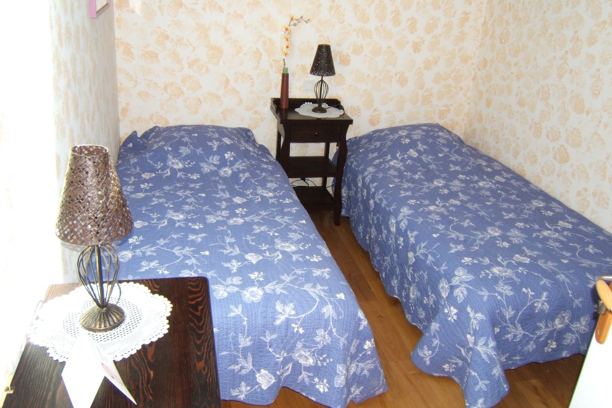 Une chambre avec deux lits, une petite table avec une lampe et un mur orné d’un motif floral.