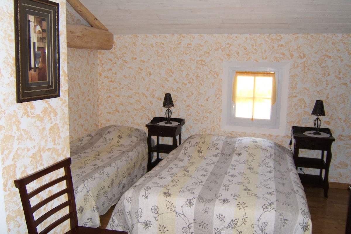 Une chambre avec deux lits, des têtes de lit en bois, une fenêtre avec des rideaux et deux tables de chevet avec des lampes.