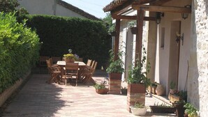A courtyard with a brick pathway, wooden furniture, and potted plants.