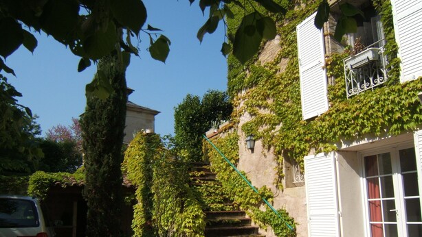 A building with a staircase surrounded by greenery, a garage, and a vehicle.