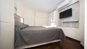 A bedroom with a bed, a flat-screen TV mounted on the wall, and an air conditioning unit.