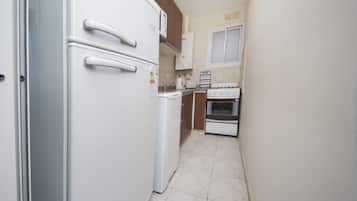 A compact kitchen with a white refrigerator, a stove, and wooden cabinets.