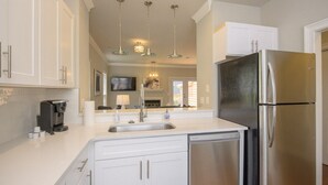 Une cuisine moderne avec des meubles blancs, des appareils en acier inoxydable et des luminaires suspendus.