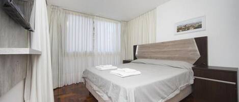 A bedroom with a bed, a TV, and a window with curtains.