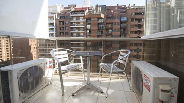 A balcony with two chairs and a table, air conditioning units, and a view of a residential area with multiple apartment buildings. - Obispo Oro Flat ZX6 (Córdoba)