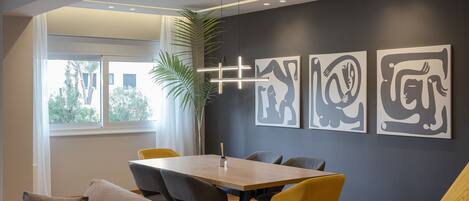 A modern dining area with a wooden table and yellow chairs, a gray sofa, and abstract wall art.