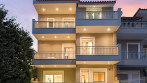 A multi-story residential building with a swimming pool, outdoor seating, and a well-lit entrance. - Athenian Grand Riviera Villa (Vari-Voula-Vouliagmeni)
