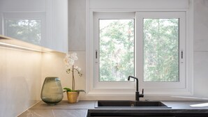 A kitchen with a modern design, featuring a double sink, a vase with flowers, and a view of greenery through the window. - Athenian Grand Riviera Villa (Vari-Voula-Vouliagmeni)