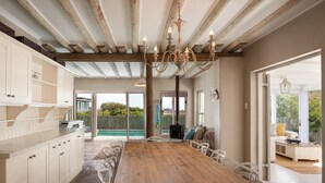 Uma cozinha espaçosa com uma mesa de madeira grande e cadeiras brancas, forno embutido e vista para uma piscina.