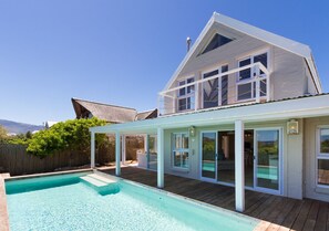 A two-story house with a swimming pool, large windows, and a covered patio area.