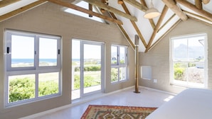 Quarto espaçoso com grandes janelas, teto de madeira e vista para o exterior.