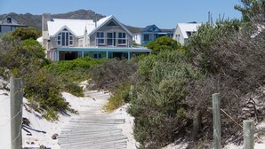 Um imóvel à beira-mar com um caminho de areia que leva a uma casa com várias janelas e telhado azul.