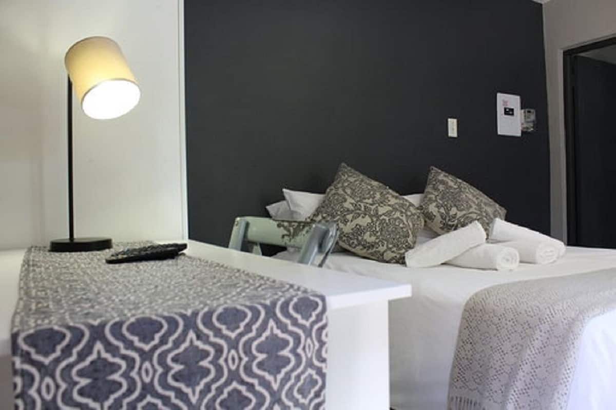 A hotel room with a bed, a bedside table with a lamp, and a patterned throw on the bed.