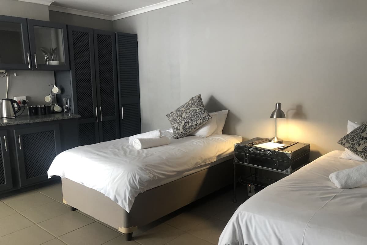 A hotel room with two beds, a kitchenette, and a bedside table with a lamp.