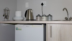 Une cuisine compacte équipée d’un réfrigérateur Hisense, d’une machine à café, d’une bouilloire et de trois récipients pour les condiments, le tout placé sur le plan de travail.