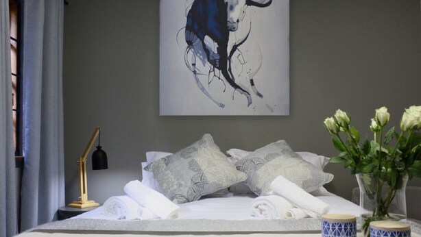 Un lit bien fait, agrémenté de coussins décoratifs, d’une lampe de chevet et d’un vase rempli de fleurs.