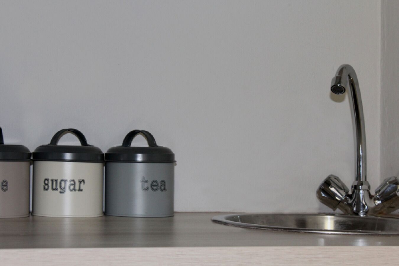 Three stainless steel containers labeled 'tea,' 'sugar,' and 'tea' on a kitchen counter.