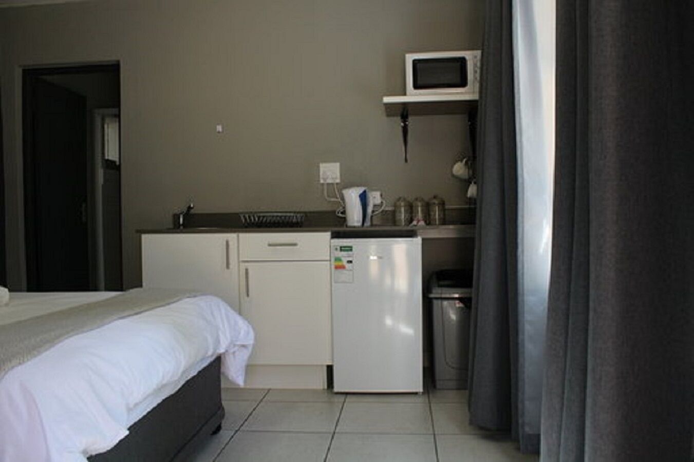Habitación de hotel compacta con cama, kitchenette, microondas y refrigerador pequeño.