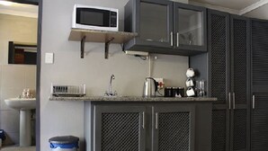 Une cuisine avec des meubles de couleur grise, un four à micro-ondes, une machine à café et une poubelle.