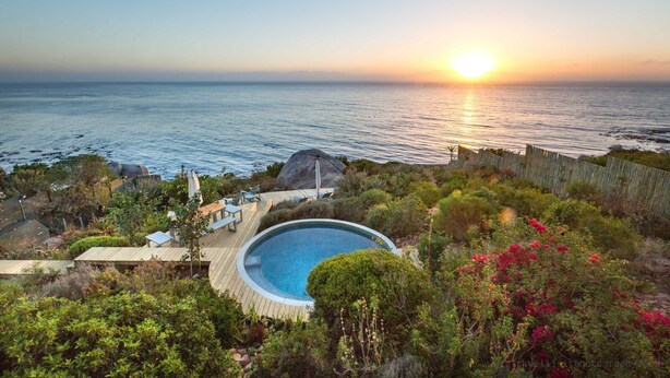 A pool surrounded by lush greenery and a wooden deck, overlooking a body of water at sunset. - Watercolours Studios (Cape Town)