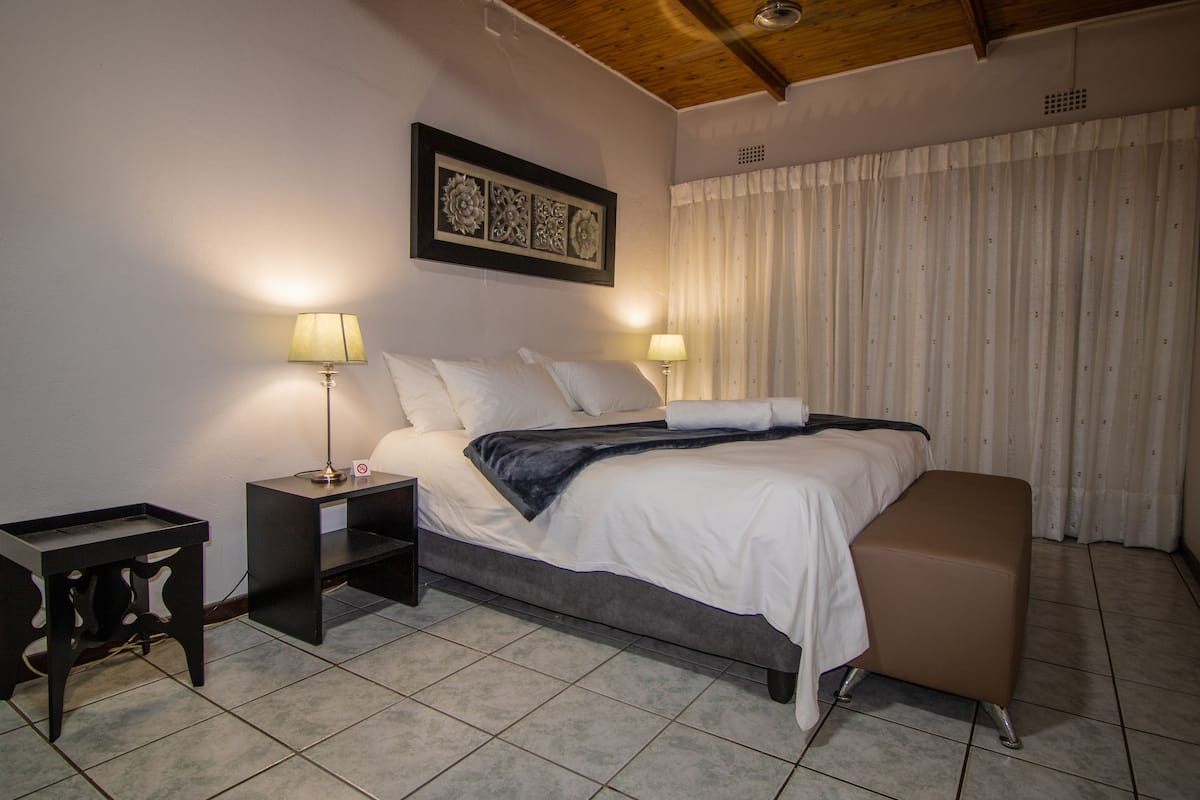 A bedroom with a bed, bedside tables, a bench, a ceiling fan, and a window with curtains.